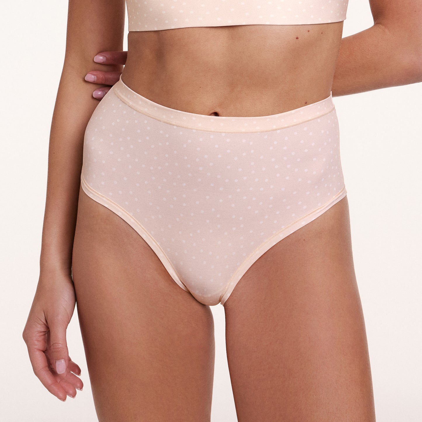 In a studio close-up, a model wears the Bliss Highwaist Brief in Champagne Fizz, showing the high-rise waistband, full coverage design, and soft microfiber fabric with a subtle dotted pattern.