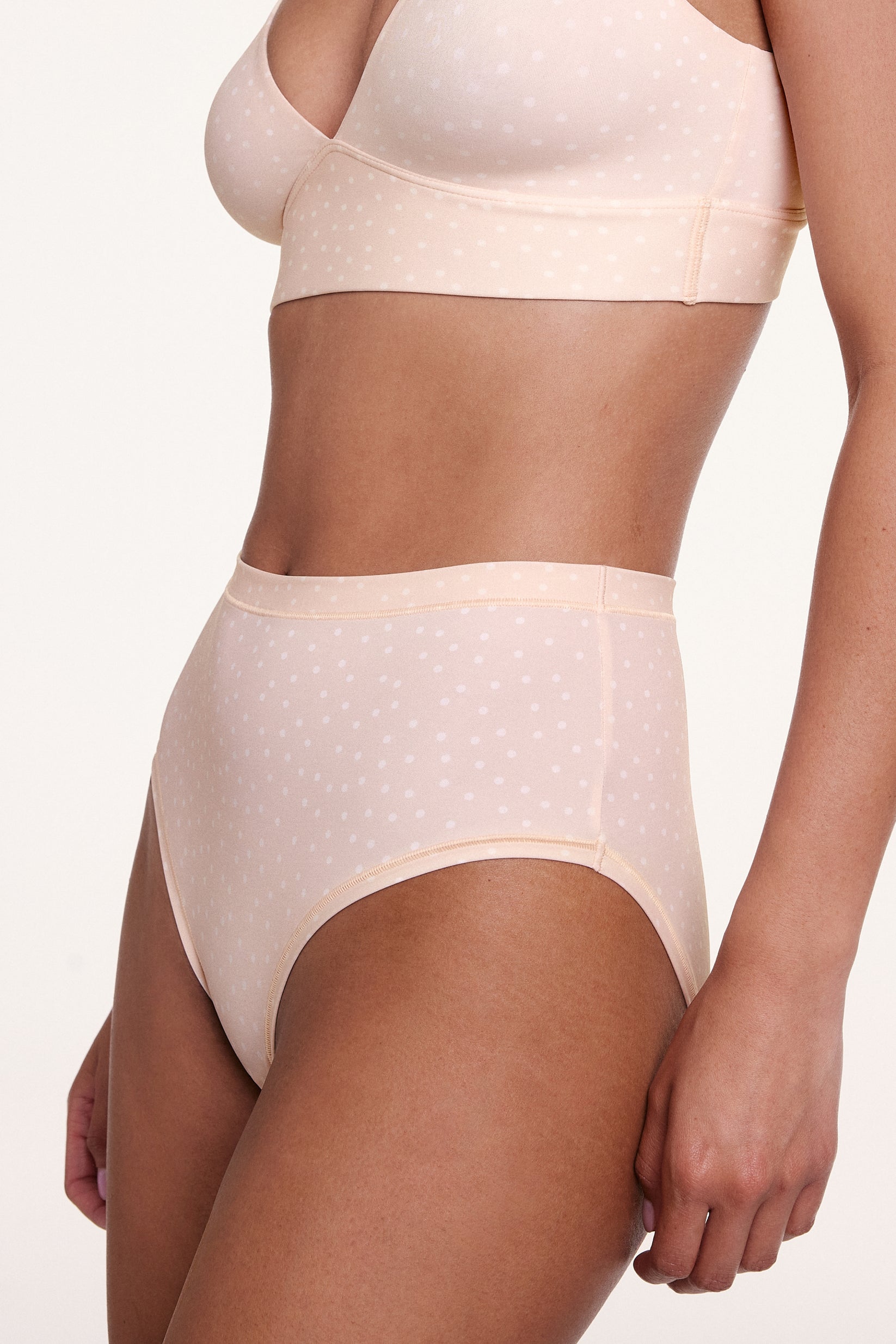 In a studio side view, a model wears the Bliss Highwaist Brief in Champagne Fizz with the Bliss Triangle Bralette in Champagne Fizz, highlighting the high-rise waistband, smooth leg openings, and soft microfiber fabric with a subtle dotted pattern. sizing: Courtney wears size Small