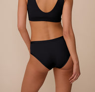 Back view of Marcela modeling the Bliss Hiphugger in Black. The full-coverage back shows the smooth, tagless design and lightweight feel of the underwear.