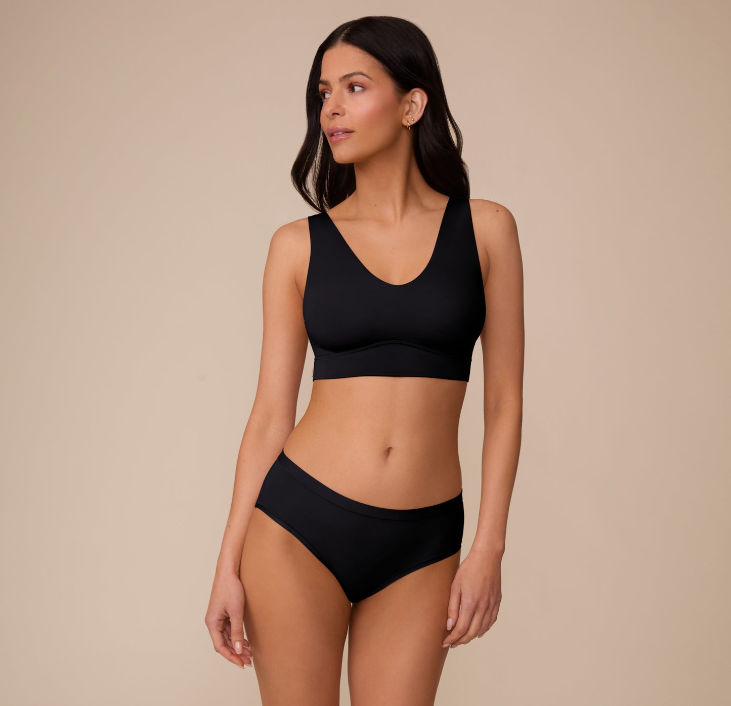 Full-body shot of Marcela wearing the Bliss Hiphugger and coordinating Bliss Bralette in Black. She stands slightly angled with a soft smile, showing the comfortable, everyday fit.