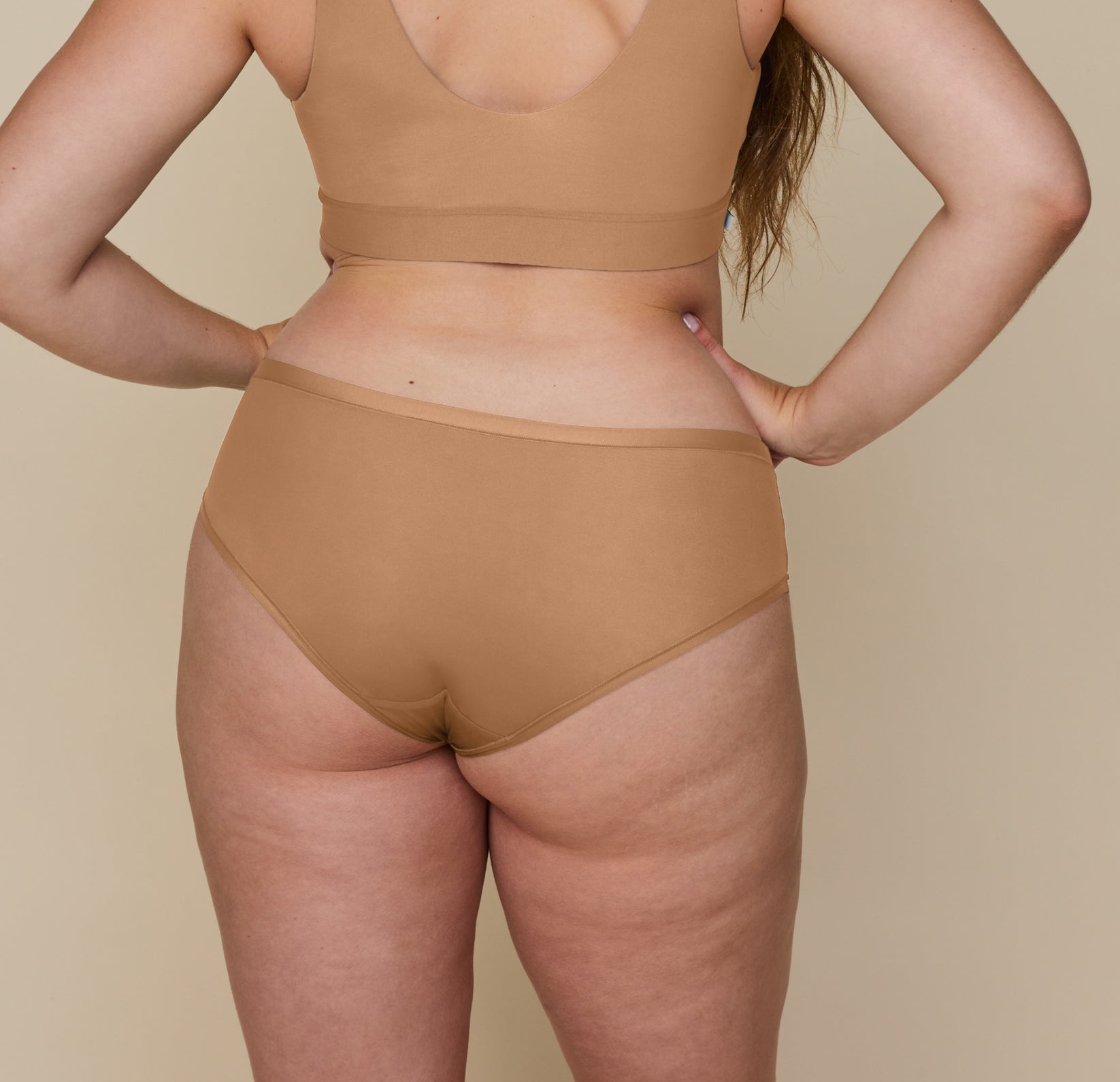 Back view of the model wearing the Bliss Bralette and Bliss HipHugger in Tan, emphasizing the coverage and comfortable feel.