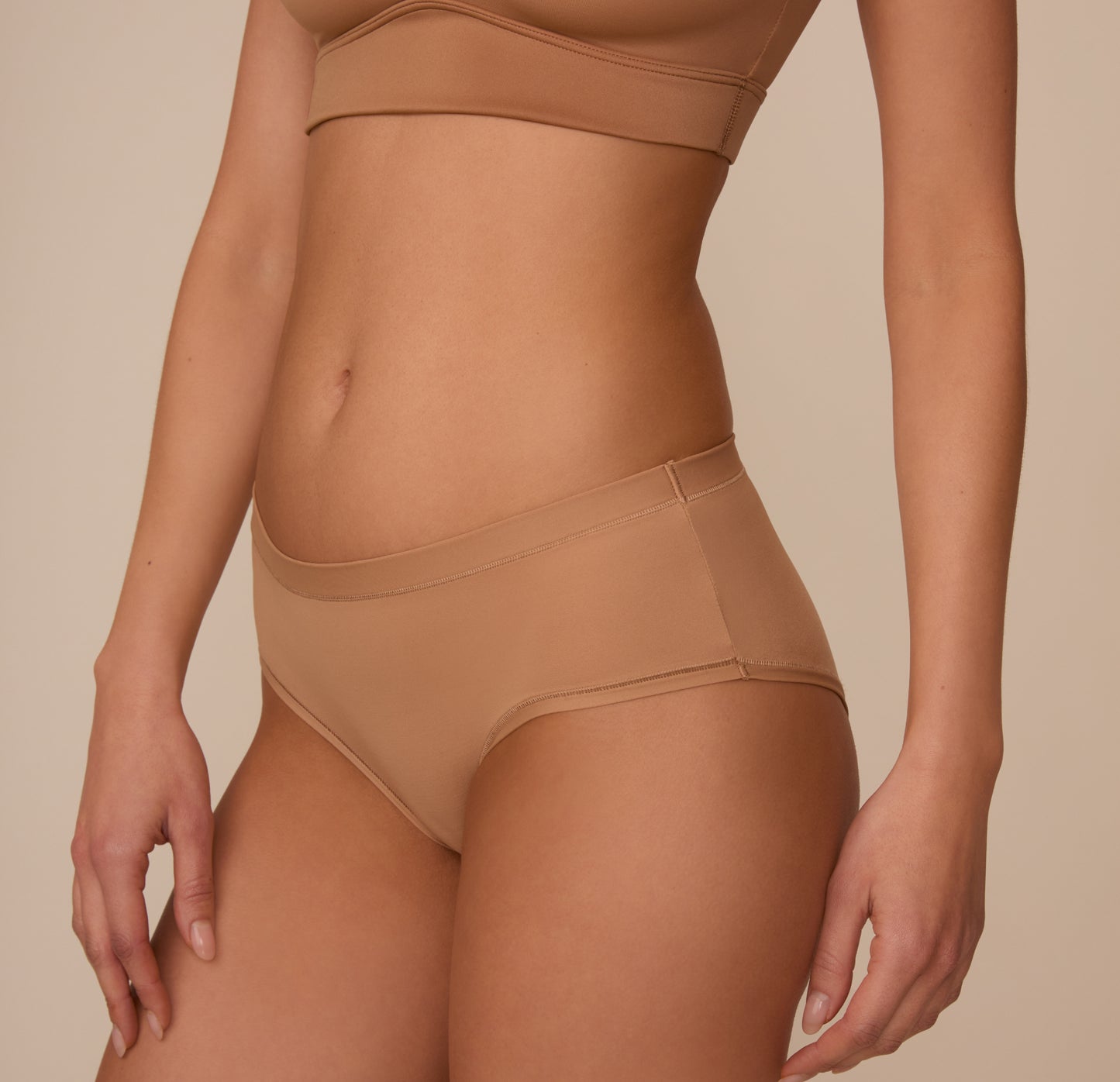 Side profile of Marcela wearing the Bliss Hiphugger in Tan, showing the soft stretch, low-rise cut, and subtle leg openings that follow the body’s natural lines.