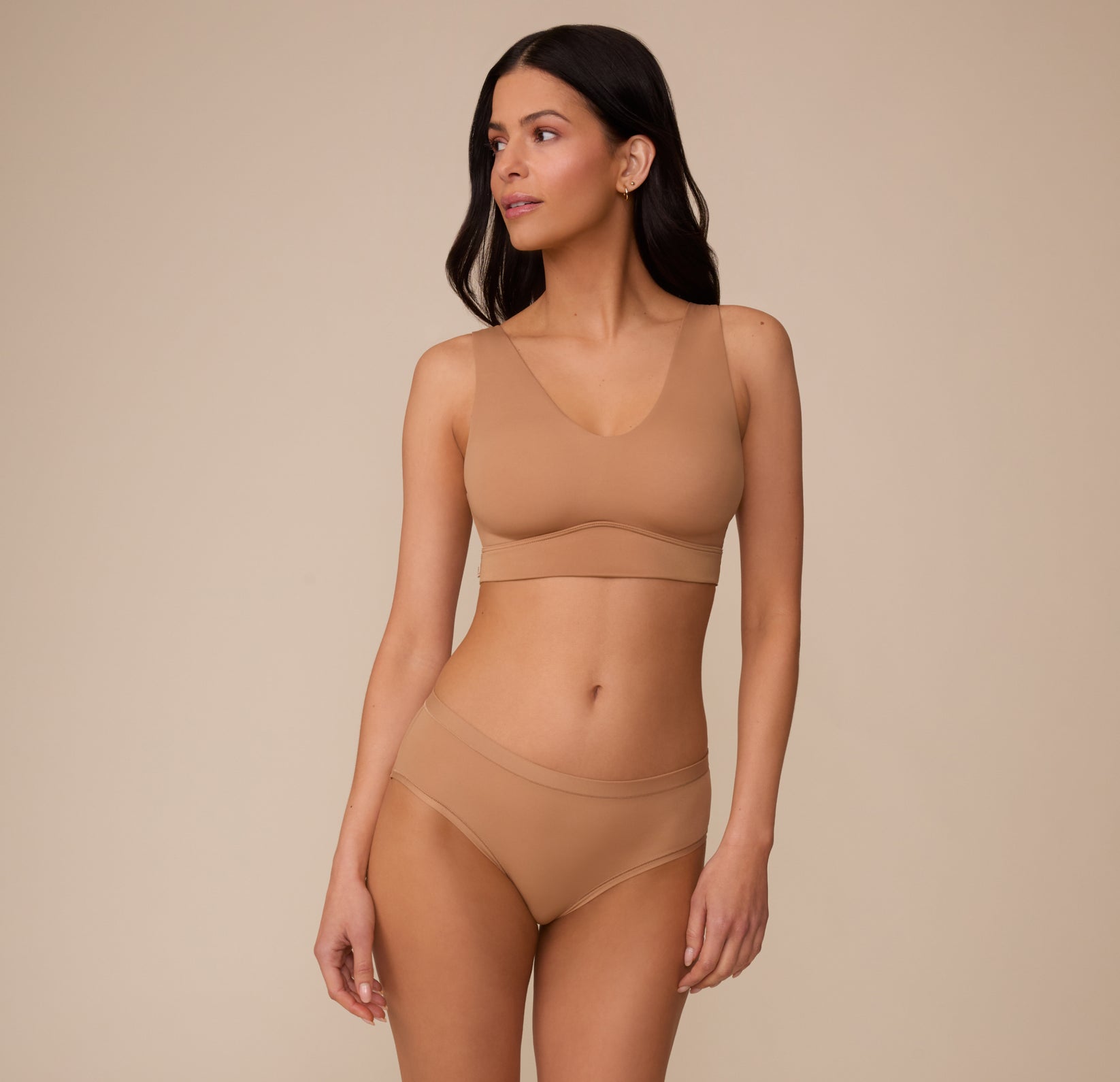 Full-body view of Marcela in the Bliss Hiphugger and the Bliss Bralette in Tan, posed in a relaxed stance. The set features a coordinated look, emphasizing comfort and simplicity.