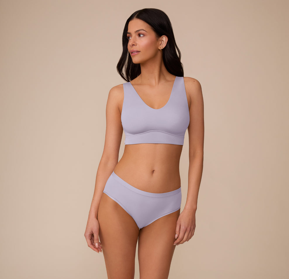 Full-body view of Marcela in the Bliss Hiphugger in Violet and the Bliss Bralette in Violet, posed in a relaxed stance. The set features a coordinated look in a soft lavender tone, emphasizing comfort and simplicity.