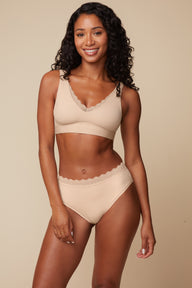 On a warm beige studio backdrop, Ally wears the Bliss Lace Bralette in Beige with matching underwear, angled front view. The bralette features a V-neckline with lace trim, smoothing sides, and a comfortable wireless band.
