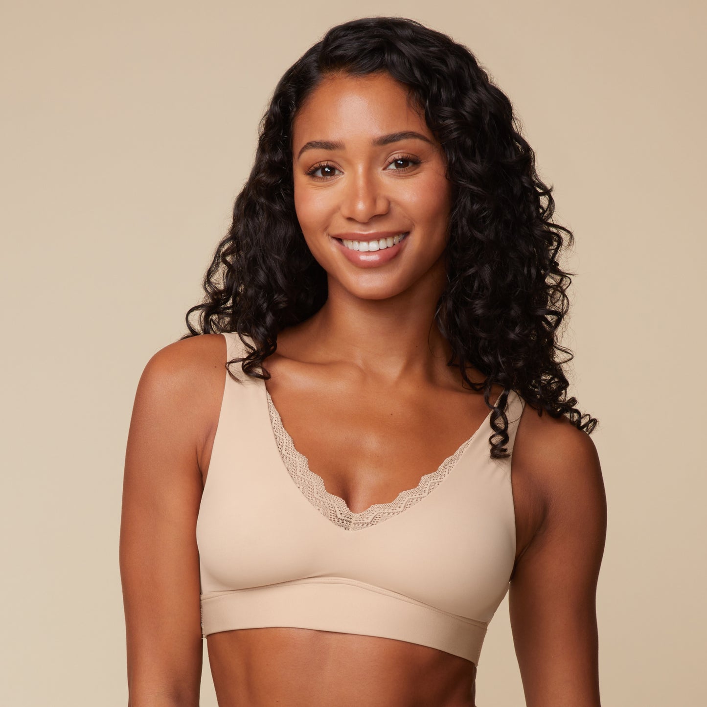 On a warm beige studio backdrop, Ally wears the Bliss Lace Bralette in Beige, front view. The ultra-soft bralette features a V-neckline with delicate lace trim and a smooth wireless band designed for everyday comfort.