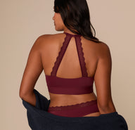 Victoria wears the Bliss Lace Halterneck Bralette in Bordeaux with a navy cardigan draped off the shoulders, showcasing the lace back design.