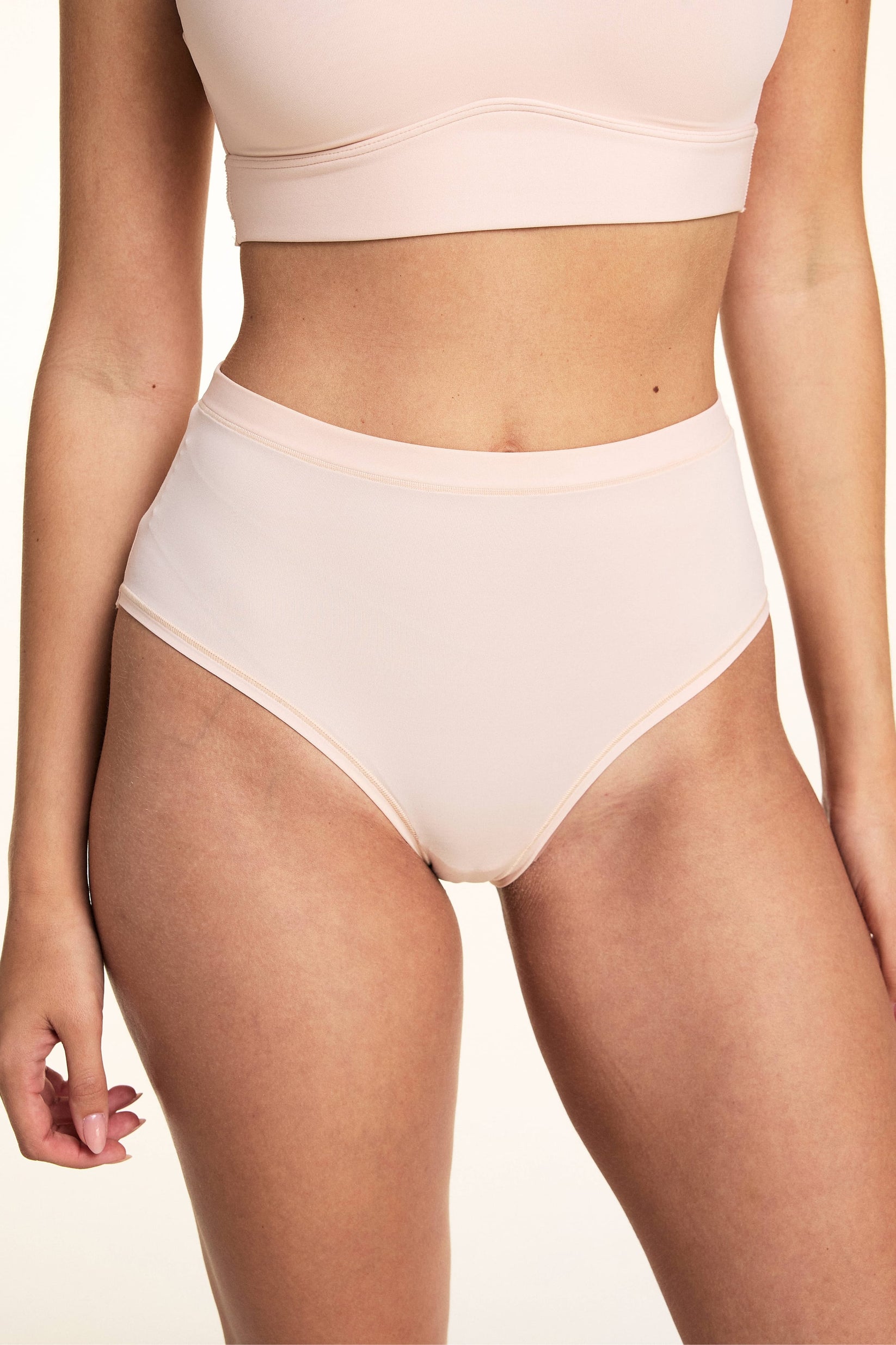 In a studio setting, Laura wears the Bliss Lace Highwaist Brief in Rose, featuring a high-rise silhouette, smooth microfiber fabric, and clean bonded edges with full front coverage.