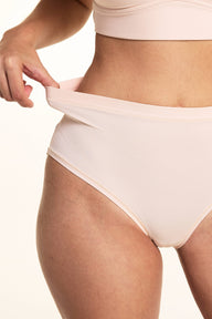 In a studio setting, Laura demonstrates the stretch waistband of the Bliss Lace Highwaist Brief in Rose, featuring smooth microfiber fabric, a high-rise silhouette, and flexible comfort.