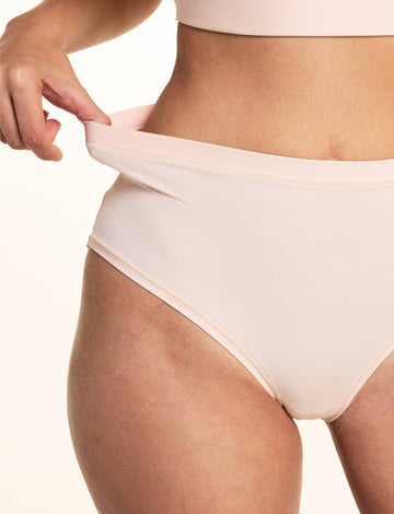 In a studio setting, Laura demonstrates the stretch waistband of the Bliss Lace Highwaist Brief in Rose, featuring smooth microfiber fabric, a high-rise silhouette, and flexible comfort.
