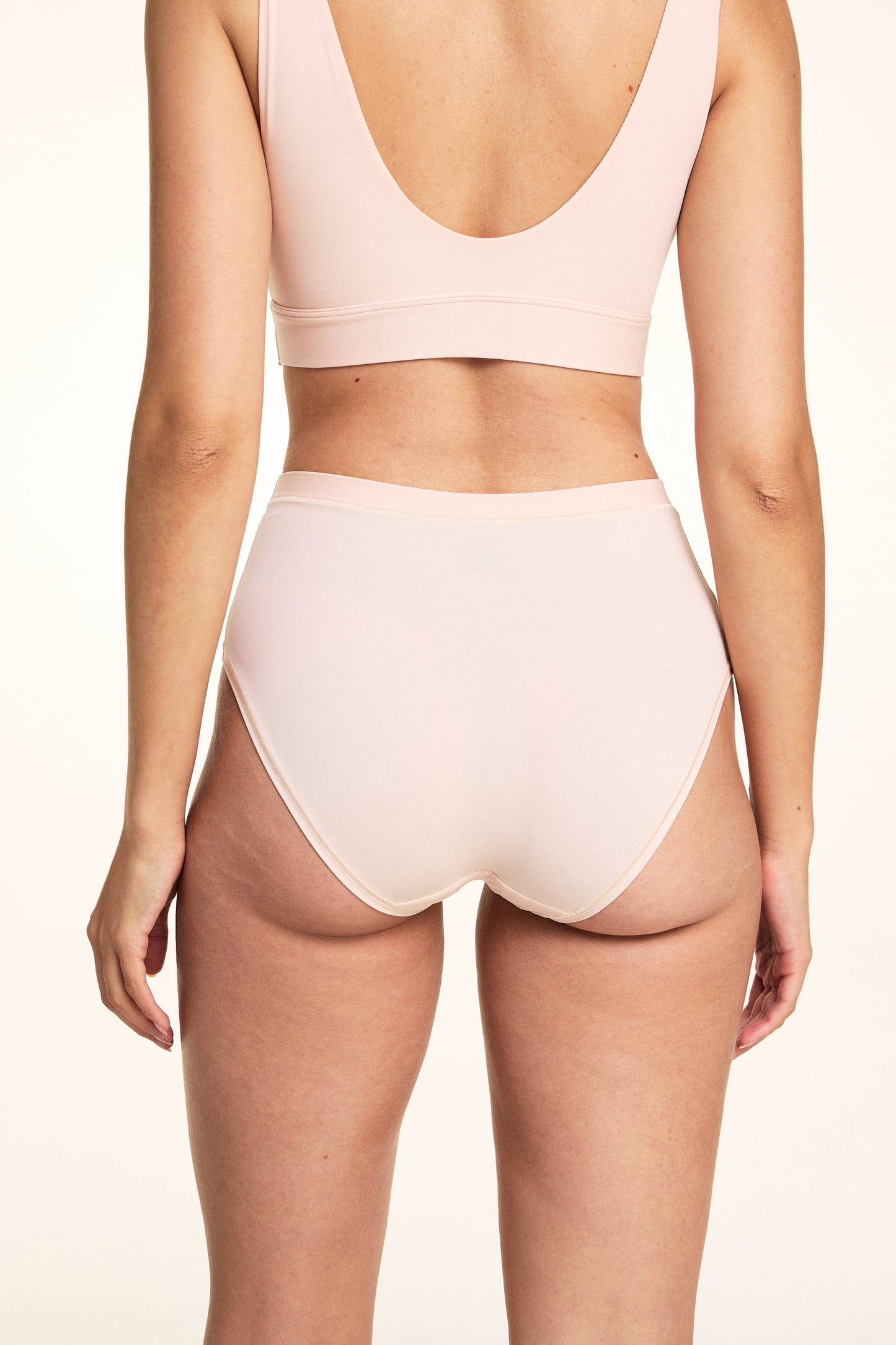 In a studio setting, Laura wears the Bliss Lace Highwaist Brief in Rose from the back, highlighting the high-rise fit, smooth microfiber fabric, and full back coverage with clean edges.