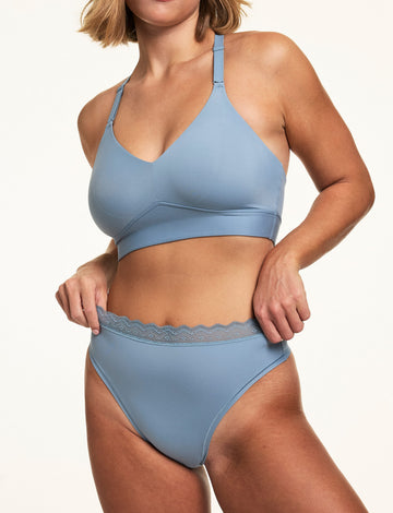 On a white studio backdrop, Sonnie wears the Bliss Lace Highwaist Thong in Poolside with a matching Poolside bralette, showing the high-rise fit and lace waistband detail. sizing: Sonnie wears size Large