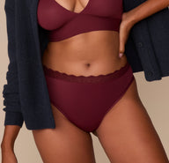 Close-up of a model wearing the Bliss Lace Highwaist Thong in Bordeaux, styled with the Bliss Halterneck Bralette and a navy cardigan. The image emphasizes the soft lace waistband .