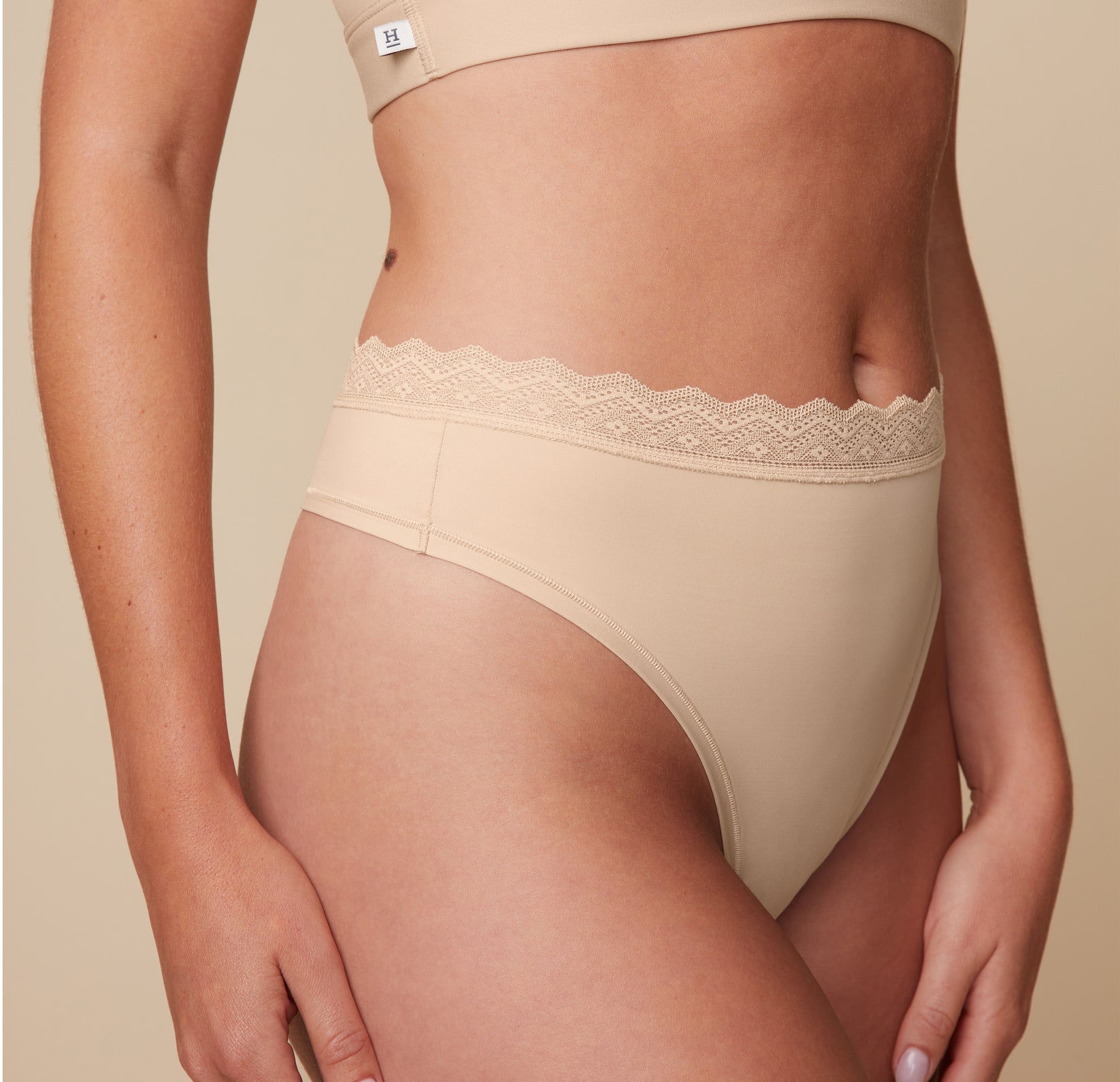 Close-up side view of the Bliss Lace Thong in Beige on Megan. The image highlights the lace waistband. sizing: Megan wears size Medium