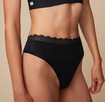 Close-up side view of Anna wearing the Bliss Lace Thong in Black. The image focuses on the delicate lace waistband. sizing: Anna wears size Small