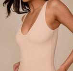 Close-up of the upper torso of the Bliss Plunge Bodysuit in Beige, focusing on the clean neckline and soft, body-hugging material worn by Marcela.