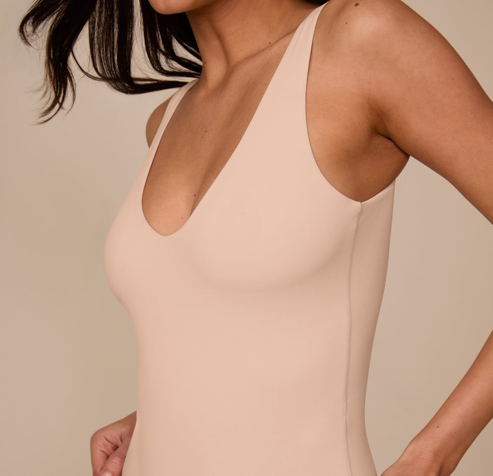 Close-up of the upper torso of the Bliss Plunge Bodysuit in Beige, focusing on the clean neckline and soft, body-hugging material worn by Marcela.
