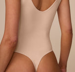 Close-up back view of Marcela wearing the Bliss Plunge Bodysuit in Beige, showing the thong-style fit and smooth scoop back design.