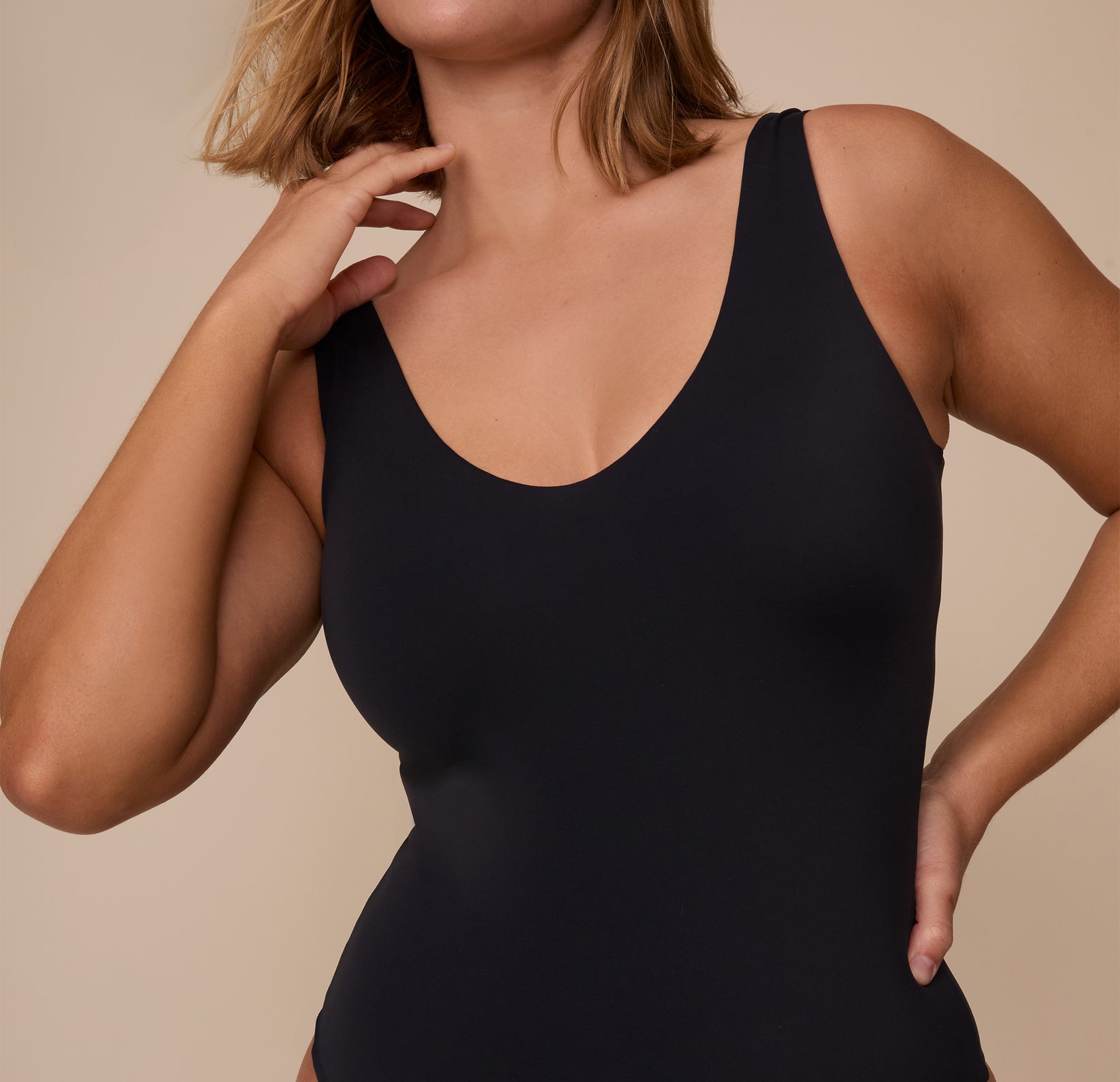 Close-up of Sonnie in the Bliss Plunge Bodysuit in Black, focusing on the deep scoop neckline and smooth microfiber fabric that hugs the body.
