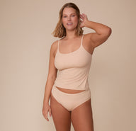 Sonnie standing in the Bliss Cami and matching Bliss Hiphugger in Beige, smiling gently. The cami’s minimal seams and clean finish are visible.
