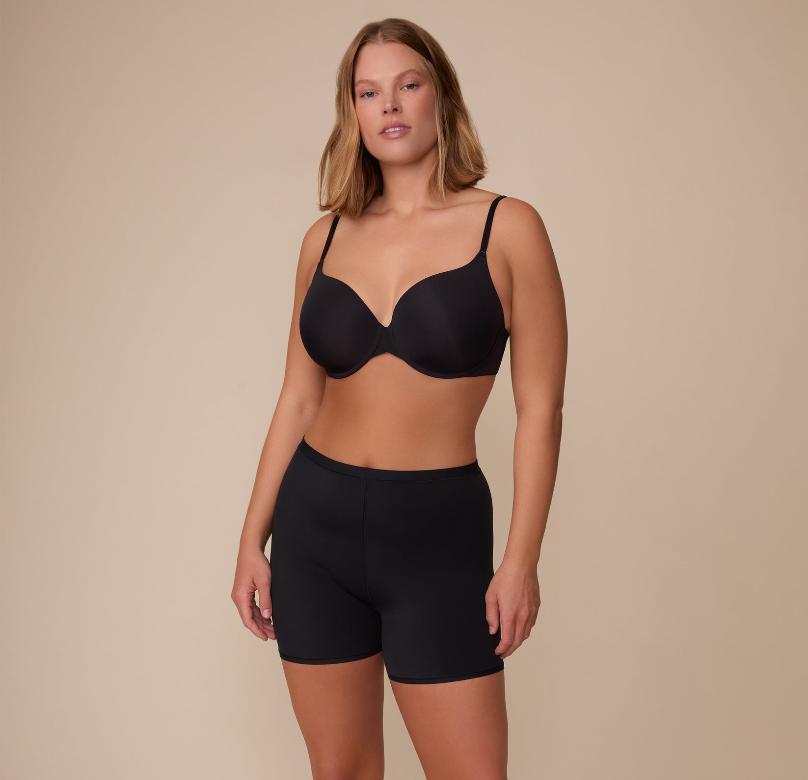 Full-body view of Sonnie wearing the Bliss Under Short and matching Base T-Shirt Bra in Black. The look showcases supportive, breathable underlayers designed for all-day ease.