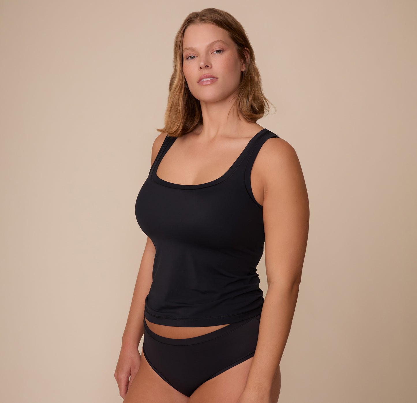 Three-quarter view of Sonnie in the Bliss Tank in Black, paired with the matching Bliss Hiphuuger in Black.The tank hugs the body for a smooth silhouette.