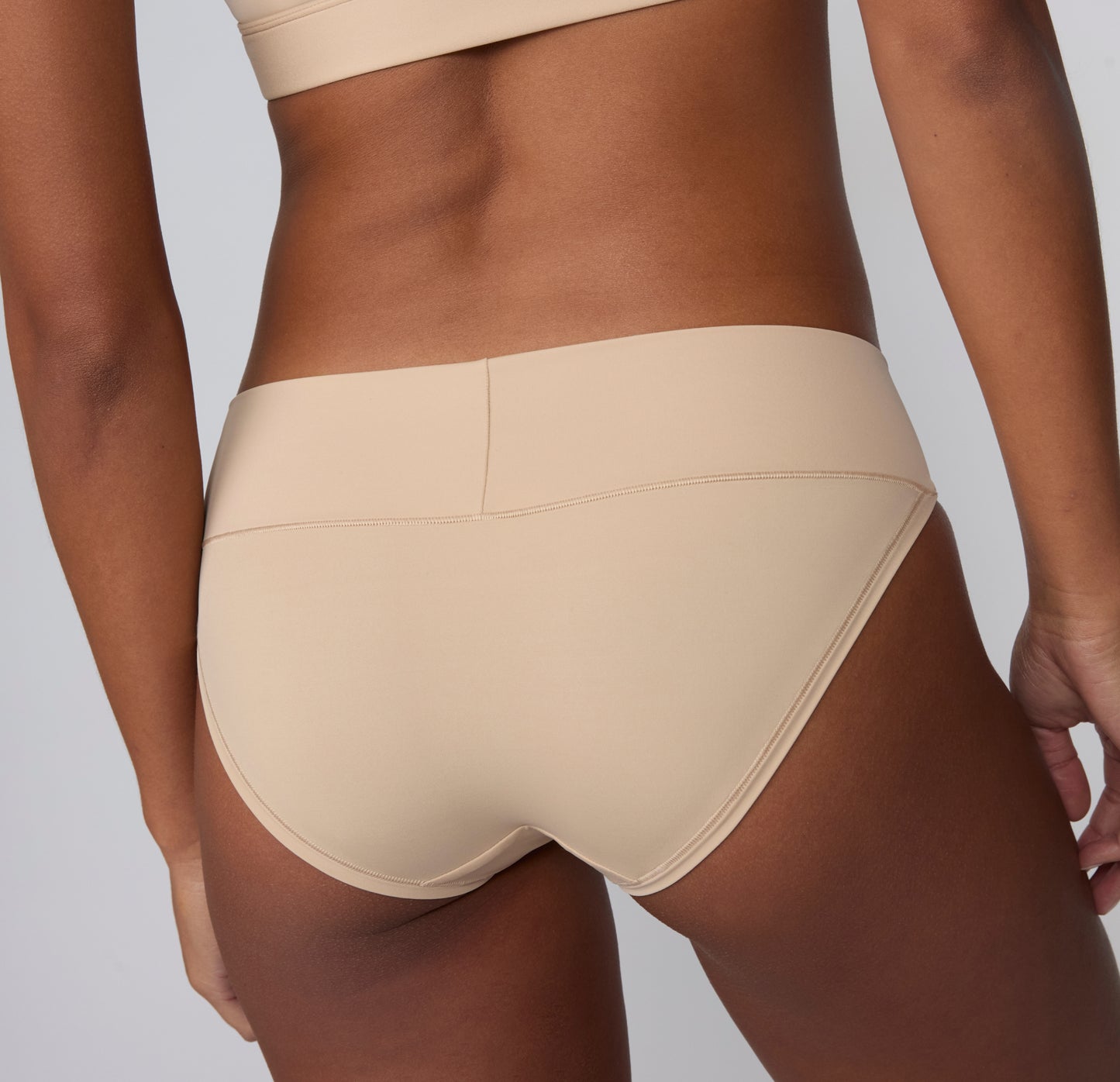 On a light gray studio backdrop, Amber wears the Bliss Low Rise Bikini in Beige, shown from the back to highlight the smooth waistband, clean stitching, and low-rise fit.