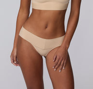 On a light gray studio backdrop, Amber wears the Bliss Low Rise Bikini in Beige, shown from the front to highlight the smooth finish, low-rise cut, and lightweight microfiber fabric.