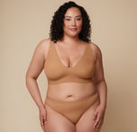 Bianca wearing the Bliss Plunge Adjustable Bralette and Bliss Thong in Tan, facing forward with hands on hips.