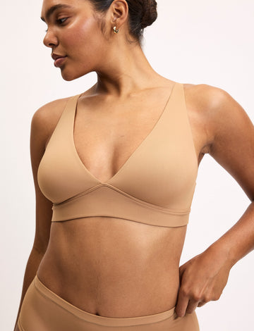Side-angle view of Amber wearing the Bliss Plunge Adjustable Bra in Tan with matching Tan underwear, showing the deep V-neckline and smooth microfiber fabric.