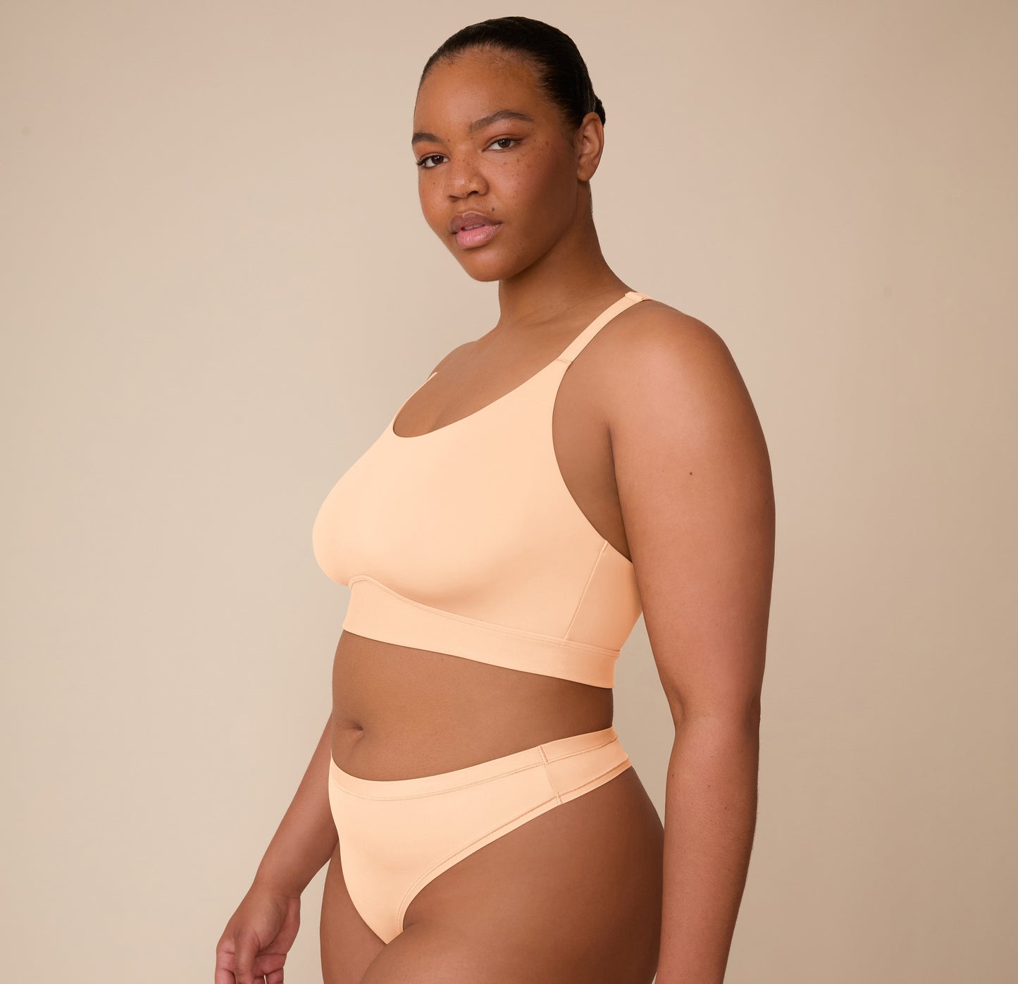 Three quarter view of Zarria wearing the Bliss Racerback Bralette and matching Bliss Thong in Daybreak, emphasizing the wide, no-dig underband and sleek fit.