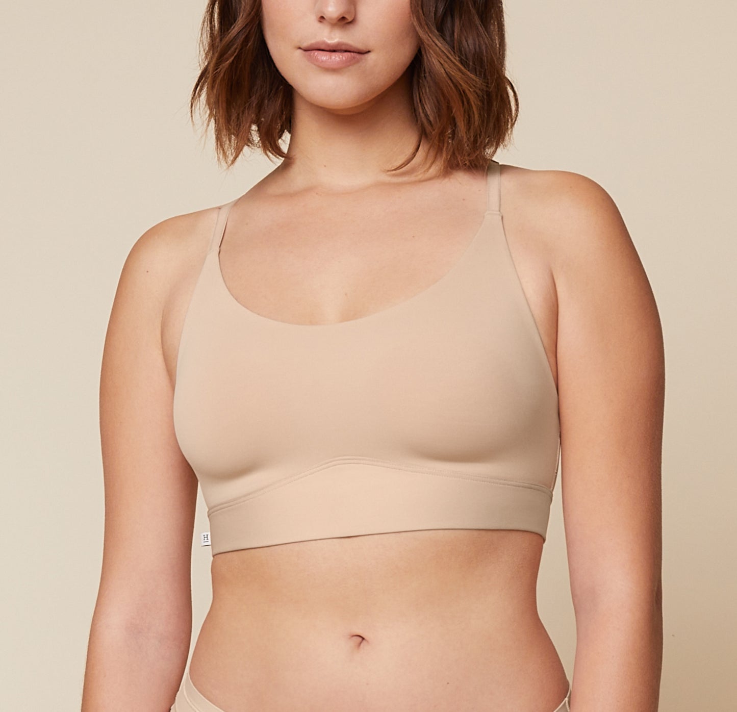 A close-up side view of Carli, focusing on her upper body. She is wearing the Bliss Racerback Bralette in Beige, showcasing the design and fit of the bralette. sizing: Carli wears size Medium