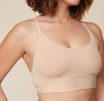 A close-up three quarter view of Carli, focusing on her upper body. She is wearing the Bliss Racerback Bralette in Beige, showcasing the design and fit of the bralette.