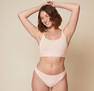 Carli standing with her arms raised, wearing the Bliss Racerback Bralette and Bliss Bikini in Rose. The front view highlights the comfortable and relaxed fit of the bralette and bikini.