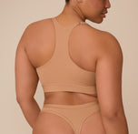 Back view of Zarria in the Bliss Racerback Bralette and Bliss Highwaist Thong in Tan. The racerback cut and wireless lift of the bralette are visible, with the thong’s high-rise design offering minimal back coverage and a smoothing fit.