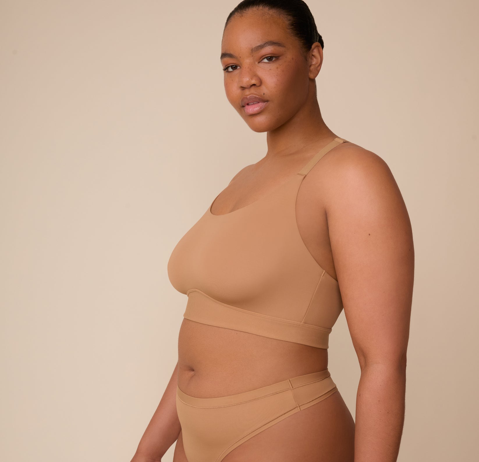 Side profile of Zarria in the Bliss Racerback Bralette and Bliss Highwaist Thong in Tan. The image highlights the thong’s high waistline and the racerback bralette’s supportive straps and smoothing fabric.