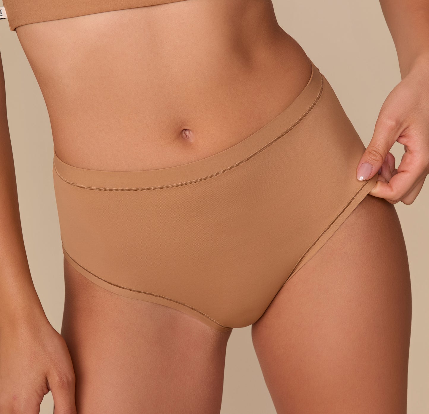 Close-up of Alexis gently pulling the fabric of the Bliss Highwaist Brief to emphasize its soft, flexible stretch and smooth finish.