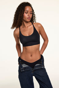 Courtney wears the Bliss Racerback Bralette in Black with matching Black underwear and relaxed-fit jeans, highlighting the racerback silhouette and soft supportive band.
