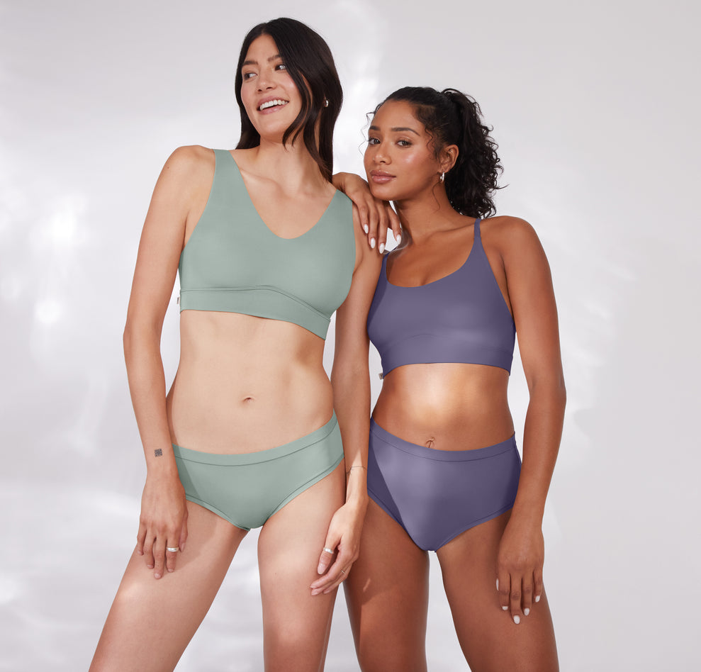 Anna and Ally pose together, wearing Bliss bralettes in complementary shades. Ally wears the Bliss Racerback Bralette in Overcast, while Anna wears the original Bliss Bralette in Seaglass, showcasing versatility in style and fit.