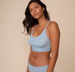 Victoria poses in a side angle wearing the Bliss Racerback Bralette in Glacier. The image highlights the minimal seam fit and soft stretch of the fabric.