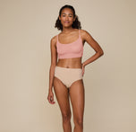 Full-body image of Zoe standing confidently, hand on her hip, in the Bliss Scoop Bralette in Dusty Rose and Bliss Highwaist Brief in Beige, showcasing the soft, relaxed fit of the matching set.