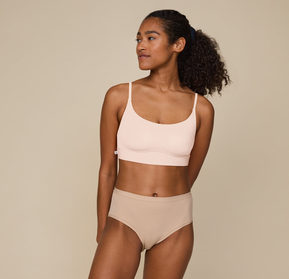 Zoe standing with hands resting at her sides, wearing the Bliss Scoop Bralette in Rose and the Bliss Highwaist Brief in Beige. She faces forward, smiling softly, showcasing the comfortable fit of both pieces. sizing: Zoe wears size Small