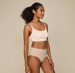 Side view of Zoe standing tall with one hand resting on her thigh, wearing the Bliss Scoop Bralette in Rose and Bliss Highwaist Brief in Beige, emphasizing the smooth, comfortable fit.