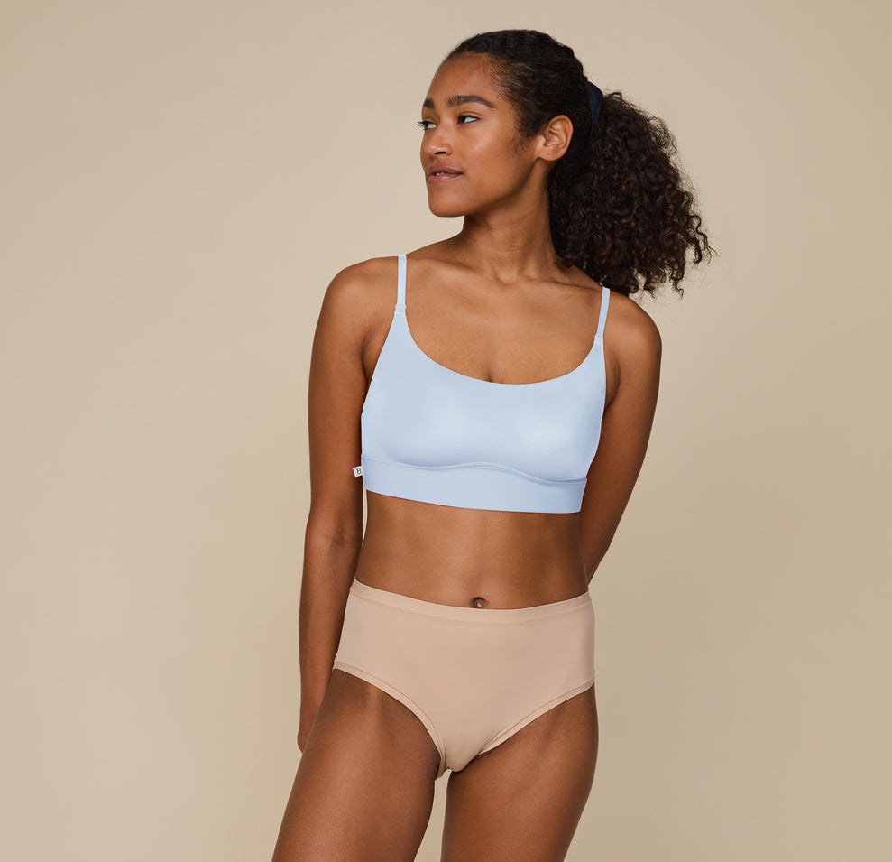 Zoe standing with hands resting at her sides, wearing the Bliss Scoop Bralette in Tidal and the Bliss Highwaist Brief in Beige. She faces forward, smiling softly, showcasing the comfortable fit of both pieces.