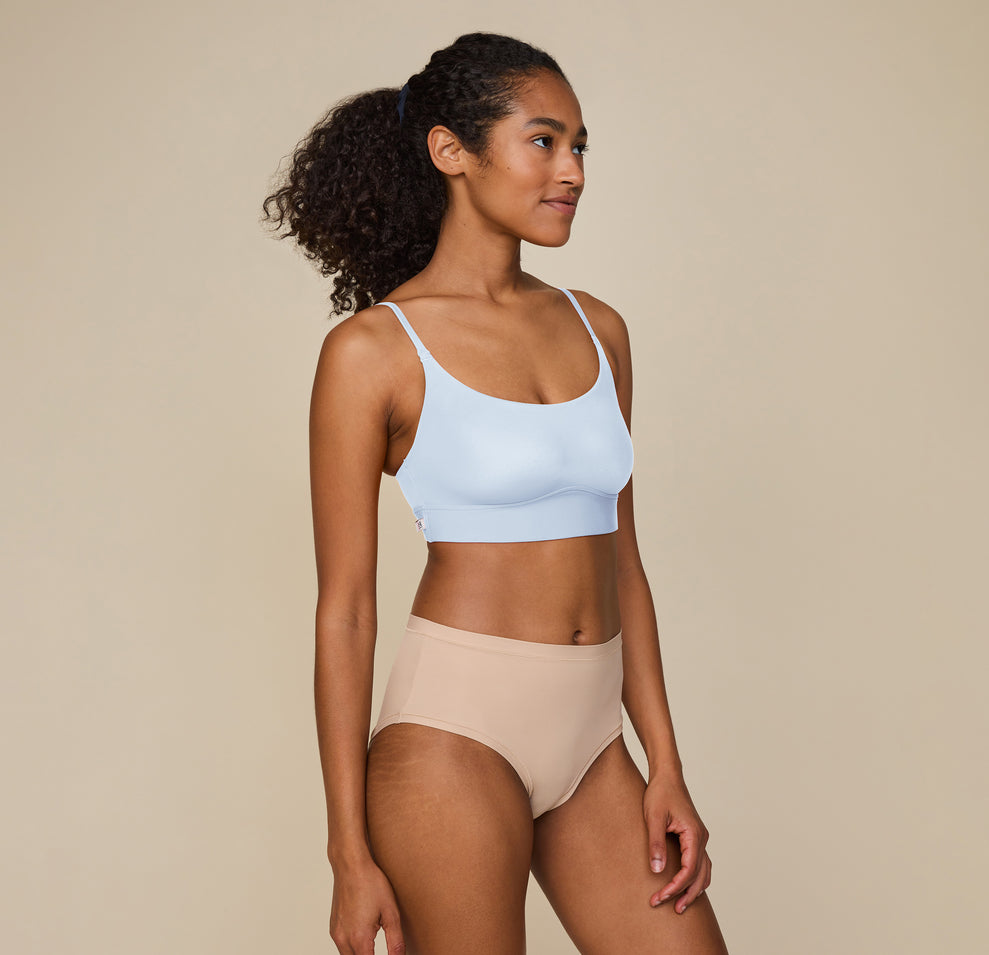 Side view of Zoe standing tall with one hand resting on her thigh, wearing the Bliss Scoop Bralette in Tidal and Bliss Highwaist Brief in Beige, emphasizing the smooth, comfortable fit. sizing: Zoe wears size Small