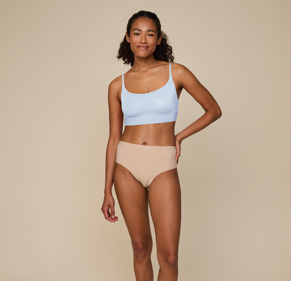 Full-body image of Zoe standing confidently, hand on her hip, in the Bliss Scoop Bralette in Tidal and Bliss Highwaist Brief in Beige, showcasing the comfortable fit of the matching set.