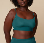 Akesha stands facing the camera, wearing the Bliss Scoop Bralette in Everglade paired with matching highwaist briefs. She smiles gently with a relaxed posture against a neutral background. sizing: Akesha wears size Large