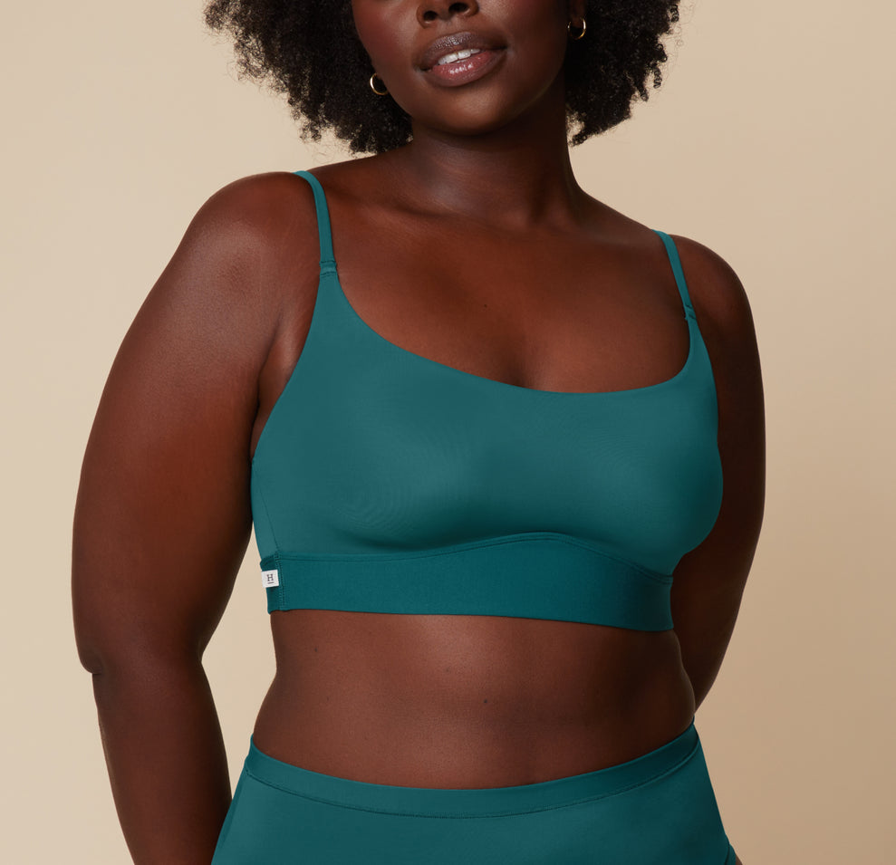Akesha stands facing the camera, wearing the Bliss Scoop Bralette in Everglade paired with matching highwaist briefs. She smiles gently with a relaxed posture against a neutral background. sizing: Akesha wears size Large