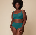 Full-body view of Akesha standing with her hands on her hips, modeling the Bliss Scoop Bralette and matching highwaist briefs in Everglade. The neutral backdrop keeps the focus on her and the fit.