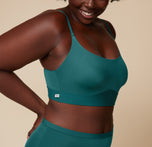 Close-up of Akesha’s upper body wearing the Bliss Scoop Bralette in Everglade. The shot captures her smile and the bralette’s simple design, set against a neutral background.